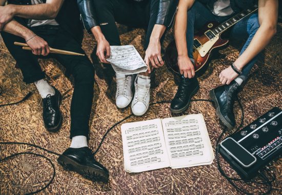 Repetition of rock music band. Cropped image of guitar players and drummer are sitting on the floor at rehearsal base with notes. Top view